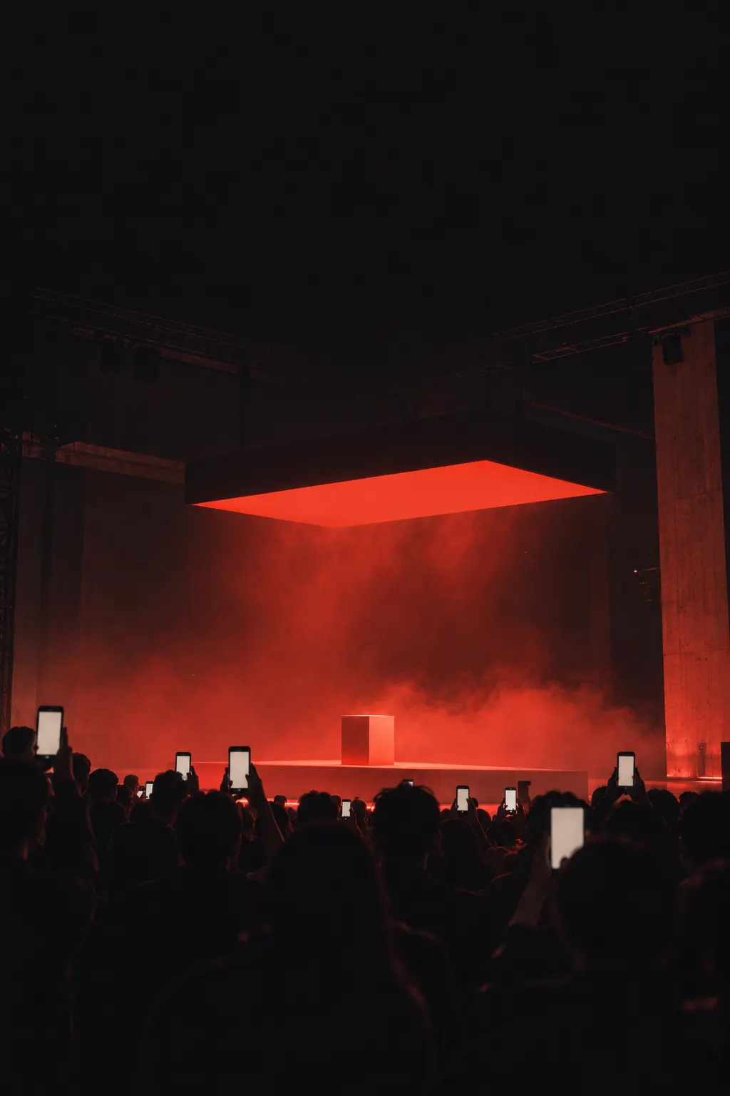 Audience silhouettes filming a red-lit launch stage on their phones